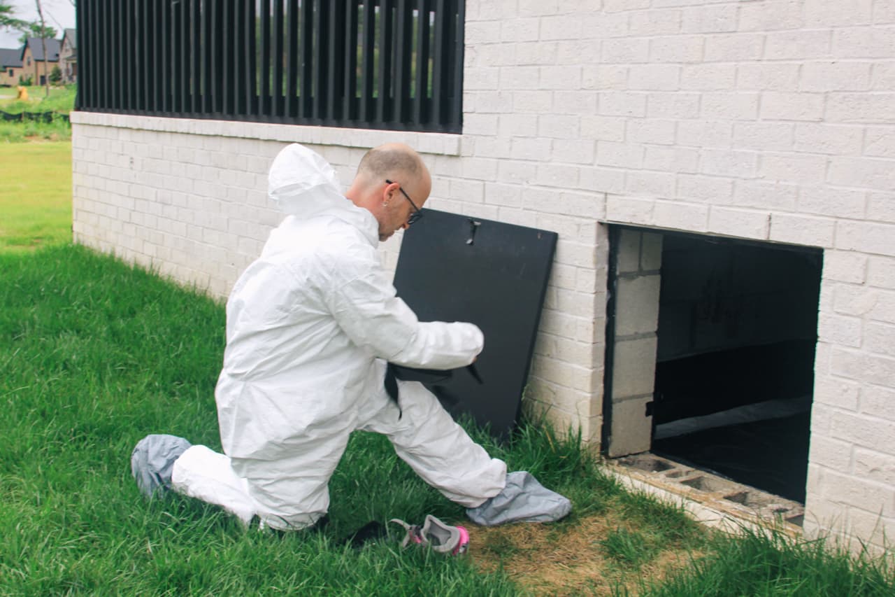 Company inspector wearing protective gear inspecting a crawlspace access opening during a termite inspection to check for wood-destroying insect activity
